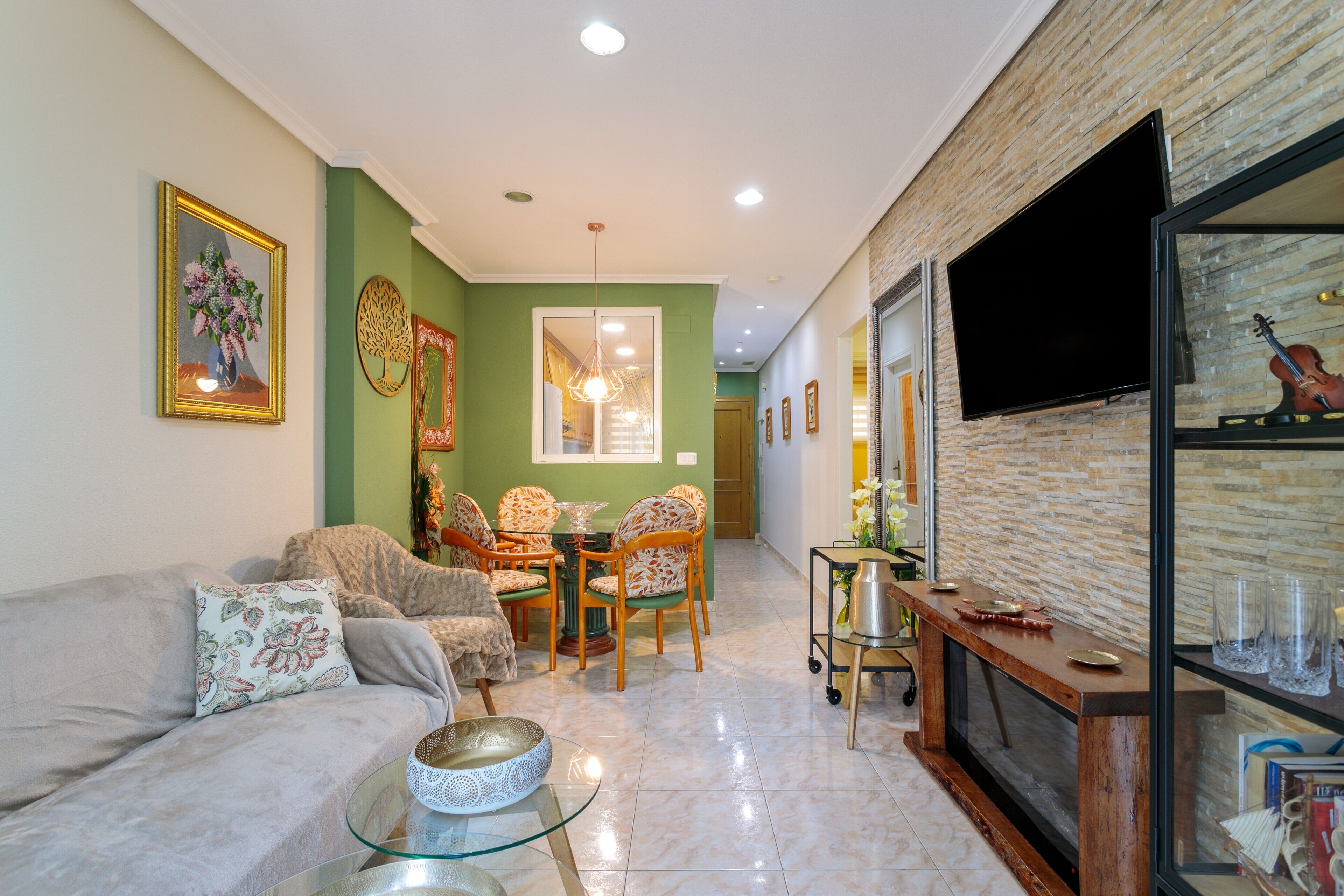 Una sala de estar con sofá, sillas, una mesa de centro de vidrio, chimenea y televisor montado en la pared.
