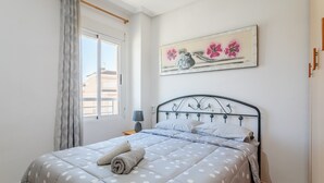 Ein ordentlich bezogenes Bett mit einem Punkte-Design-Überwurf, einer Nachttischlampe und einem Blumenbild an der Wand.