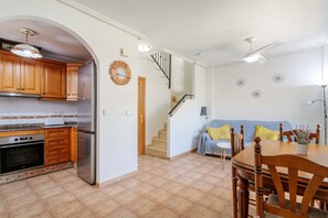 A kitchen with wooden cabinets, a refrigerator, and a built-in oven. There is a dining area with a wooden table and chairs. - Bungalow 'Adelina En Santa Pola' with Private Terrace, Wi-Fi and Air Conditioning (Santa Pola)