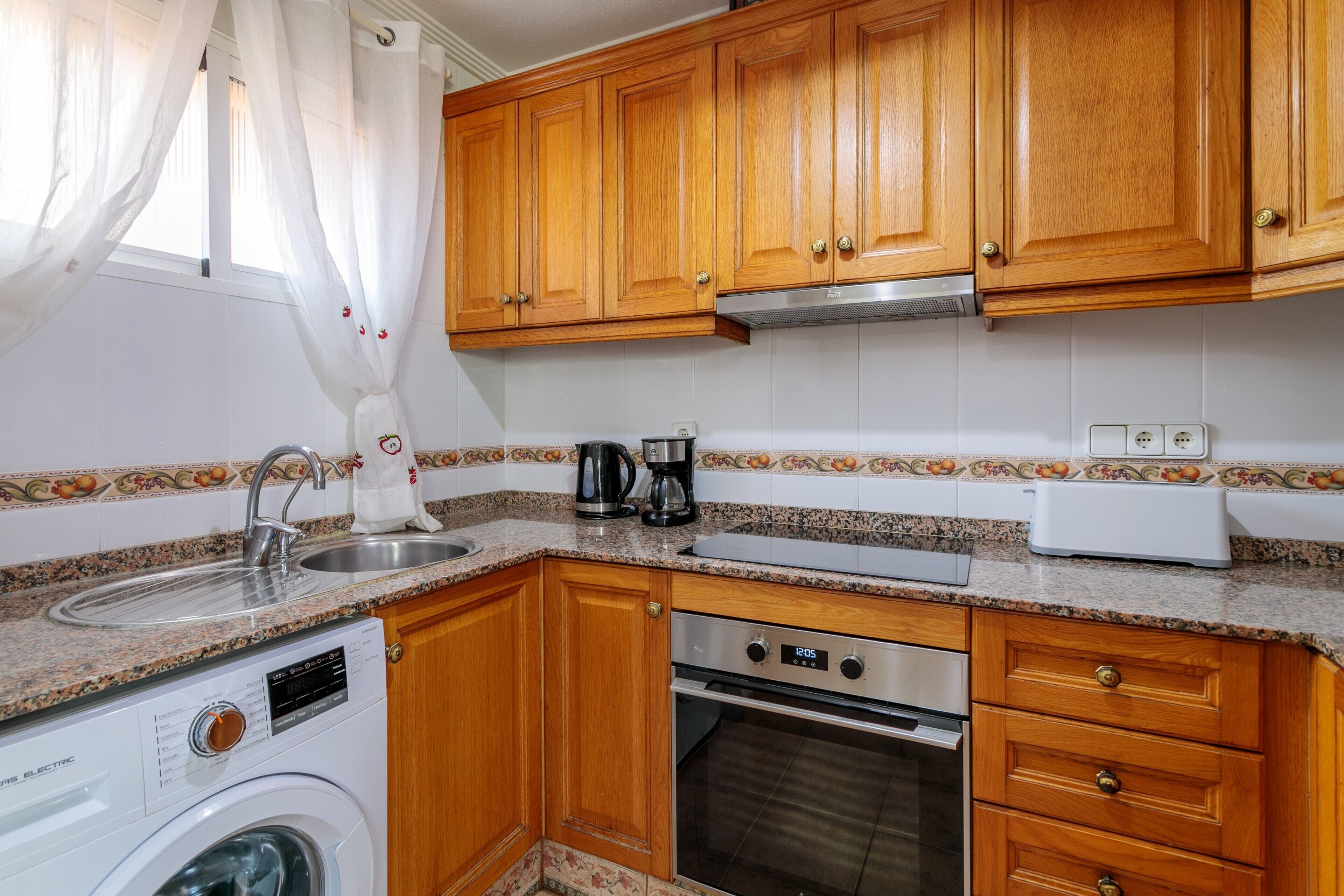 A compact kitchen with wooden cabinets, a built-in washing machine, a coffee maker, and a toaster.