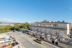 Um edifício com várias andares e varandas, com uma rua na frente e um carro amarelo estacionado.