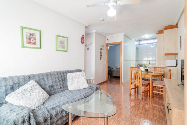 A living room with a sofa, a glass coffee table, and a dining area with a table and chairs.