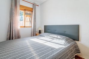 Une chambre à coucher avec un lit, une fenêtre avec des rideaux, une lampe de chevet et une tête de lit.