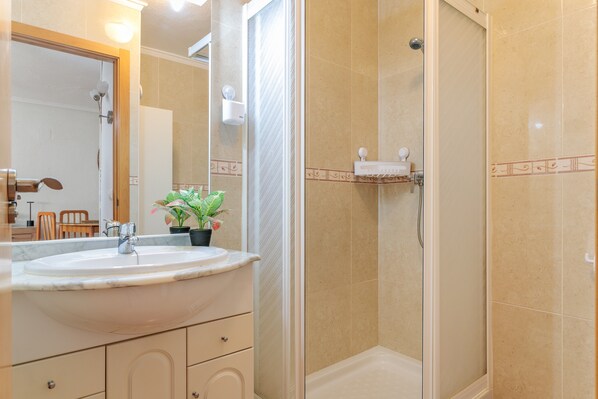 Un baño con lavamanos, espejo, ducha y una planta en maceta.