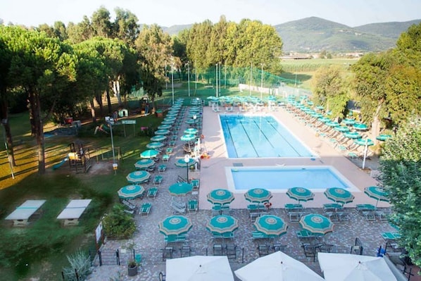 A pool area with multiple lounge chairs and umbrellas, surrounded by trees and a view of hills.