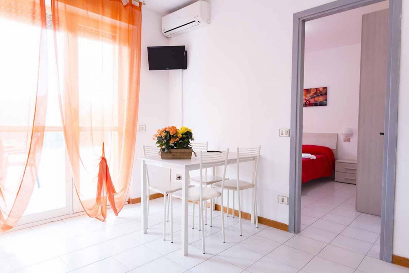 A room with a dining table, chairs, a TV, and a bed with a red bedspread.