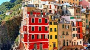 A colorful coastal building with multiple balconies and a steep, rocky cliff. - Two-room apartment of 45 sqm, consisting of a large living room/dining area with equipped kitchenette and sofa bed with 2 single pull-out beds, a double bedroom, bathroom with shower, private balcony complete with table and chairs.Equipped with:- Air con (Luni Mare)