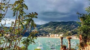 A coastal view with boats docked at a marina, surrounded by greenery and hills. - Two-room apartment of 45 sqm, consisting of a large living room/dining area with equipped kitchenette and sofa bed with 2 single pull-out beds, a double bedroom, bathroom with shower, private balcony complete with table and chairs.Equipped with:- Air con (Luni Mare)