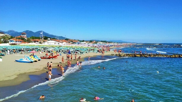 A crowded beach with people swimming and sunbathing, a lifeguard tower, and a rocky breakwater. - Two-room apartment of 45 sqm, consisting of a large living room/dining area with equipped kitchenette and sofa bed with 2 single pull-out beds, a double bedroom, bathroom with shower, private balcony complete with table and chairs.Equipped with:- Air con (Luni Mare)