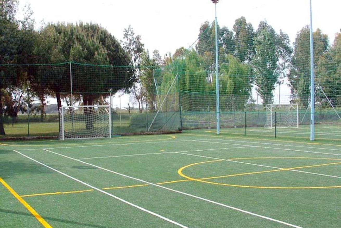 An outdoor tennis court with a net, goalpost, and surrounding trees.