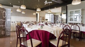 En restaurant med runde borde, røde stole og hængende fletlamper.