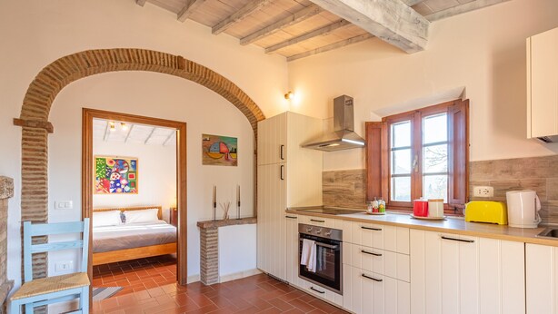 A kitchen with white cabinets, a stove, a window, and a door leading to a bedroom. - Apartment 'Casamoira' with Private Terrace, Wi-Fi and Air Conditioning (Trequanda)