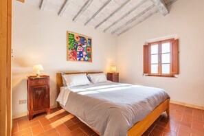 Une chambre à coucher comprenant un lit, une table de chevet, une œuvre d’art murale, une fenêtre et un plafond en bois.