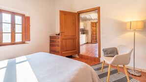 A bedroom with a bed, wooden wardrobe, a chair, a floor lamp, and a view of the kitchen through an open door. - Apartment 'Casamoira' with Private Terrace, Wi-Fi and Air Conditioning (Trequanda)