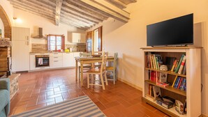 A cozy living room with a fireplace, a dining area with a table and chairs, a bookshelf, and a television. - Apartment 'Casamoira' with Private Terrace, Wi-Fi and Air Conditioning (Trequanda)