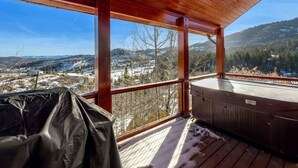 Eine Holzterrasse mit Whirlpool, überdachtem Grill und Blick auf eine verschneite Landschaft.