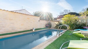 A swimming pool with a stone wall, a wooden deck, and a metal ladder.