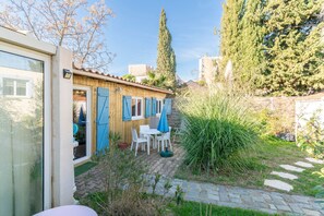 A wooden building with a patio area, including a table and chairs, and a door with blue shutters. - Holiday Home 'Le Chalet Houda Et Spa En Option' with Private Pool and Air Conditioning (Nîmes)