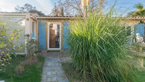A house with a stone pathway leading to a door, surrounded by greenery and a clear sky.