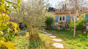 A garden with a stone pathway leading to a wooden house with blue shutters.