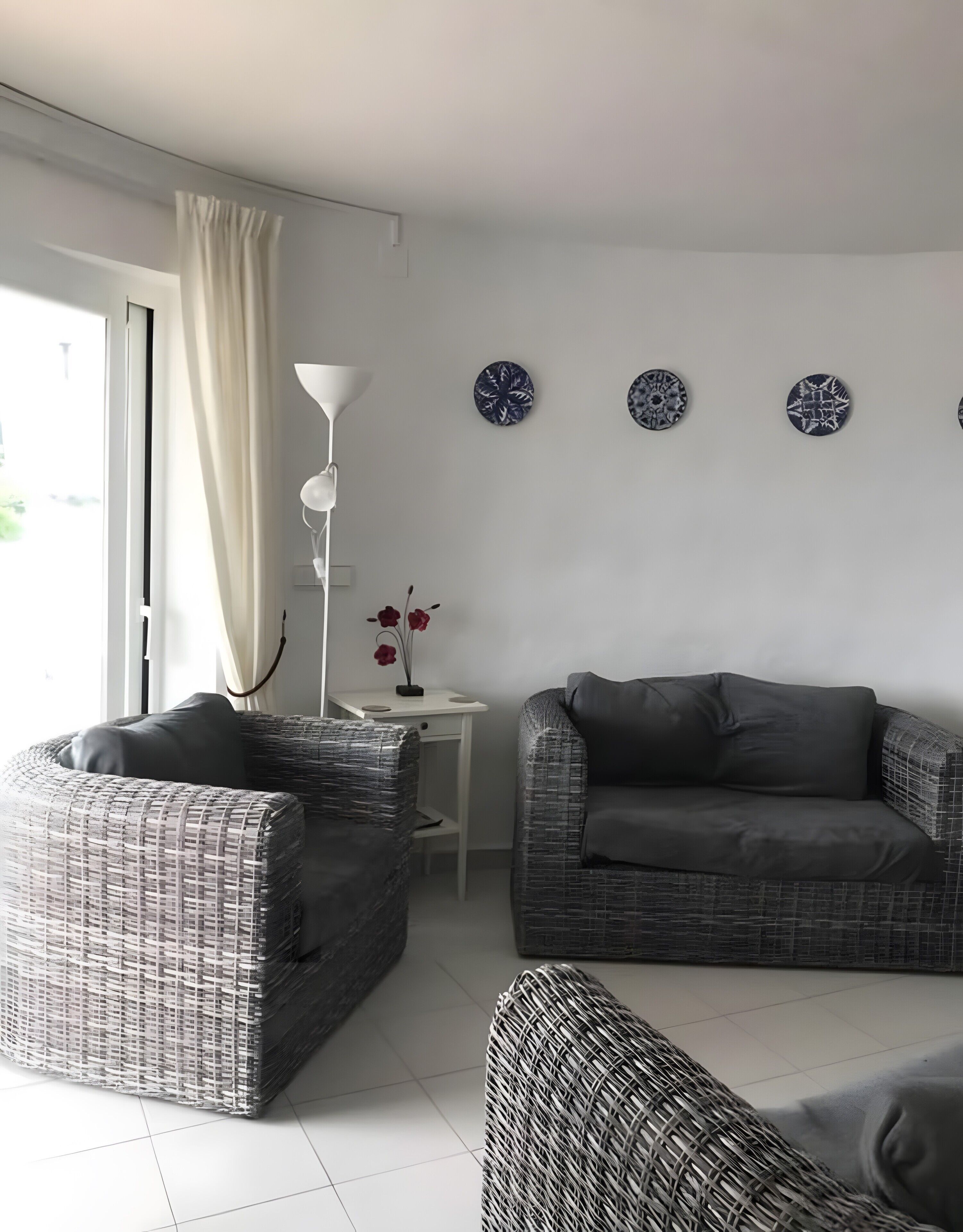A living room with wicker furniture, a white table, a floor lamp, and decorative plates on the wall.