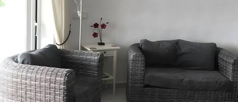 A living room with wicker furniture, a white table, a floor lamp, and decorative plates on the wall.