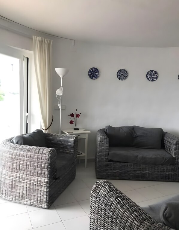 A living room with wicker furniture, a white table, a floor lamp, and decorative plates on the wall. - Villa 'Las Amapolas' with Private Pool, Wi-Fi and Air Conditioning (Cala en Porter)