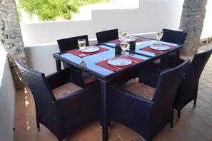 A dining table set with plates, cutlery, and glasses, surrounded by wicker chairs. - Villa 'Las Amapolas' with Private Pool, Wi-Fi and Air Conditioning (Cala en Porter)
