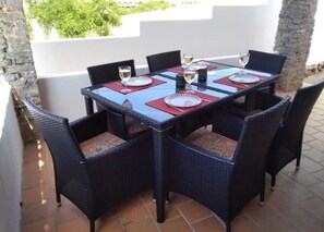 Mesa preparada para seis personas con sillas de mimbre, patio exterior y vista a zonas verdes.