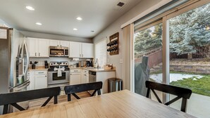 A modern kitchen with white cabinets, stainless steel appliances, and a dining area with a wooden table and chairs. - Quartz Castle (Castle Rock)