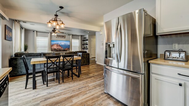 A modern kitchen with a stainless steel refrigerator, a dining area with a wooden table and chairs, and a ceiling fan. - Quartz Castle (Castle Rock)