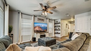 A living room with a large gray sectional sofa, a ceiling fan, a flat-screen TV, and a fireplace. - Quartz Castle (Castle Rock)