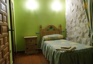 A bedroom with a bed, a nightstand, a wooden wardrobe, and a stone wall.