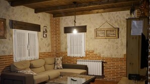 Ein Wohnzimmer mit einer Couch, einem Glastisch, einer Pendelleuchte, einer Heizung und einer Ziegelwand.