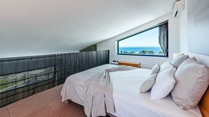 Une chambre d’hôtel moderne dotée d’un grand lit, offrant une vue sur la mer et disposant d’un balcon avec une rambarde en métal.