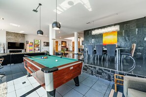 Una mesa de billar en un salón moderno con un muro de piedra decorativa y muebles contemporáneos.