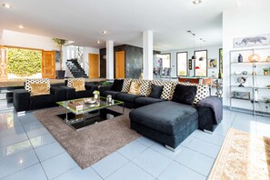 Una sala de estar moderna con un sofá modular, una mesa de centro de vidrio y una escalera que lleva a un nivel superior.