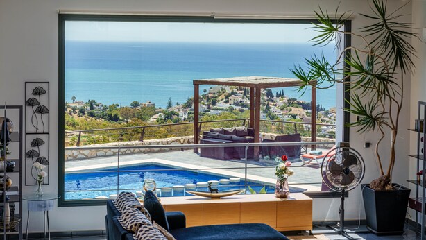 Un salon moderne doté d’une grande fenêtre donnant sur une piscine et la mer.