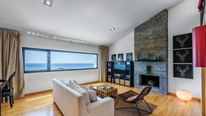 Un salon moderne avec un canapé, un téléviseur, une cheminée en pierre et une grande fenêtre donnant sur la mer.