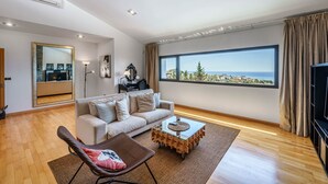 Un salon moderne comprenant un canapé, une table basse en verre, un fauteuil, une grande fenêtre offrant une vue dégagée et un téléviseur à écran plat.