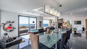 Un salon moderne avec une table à manger en verre, des sièges confortables, une vue sur la piscine et une grande fenêtre.