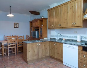 A kitchen with wooden cabinets, a built-in microwave, a white dishwasher, and a dining area with wooden chairs and a table.