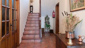 Un escalier menant à un palier où se trouvent un extincteur, un tableau encadré et un vase contenant des plantes séchées.