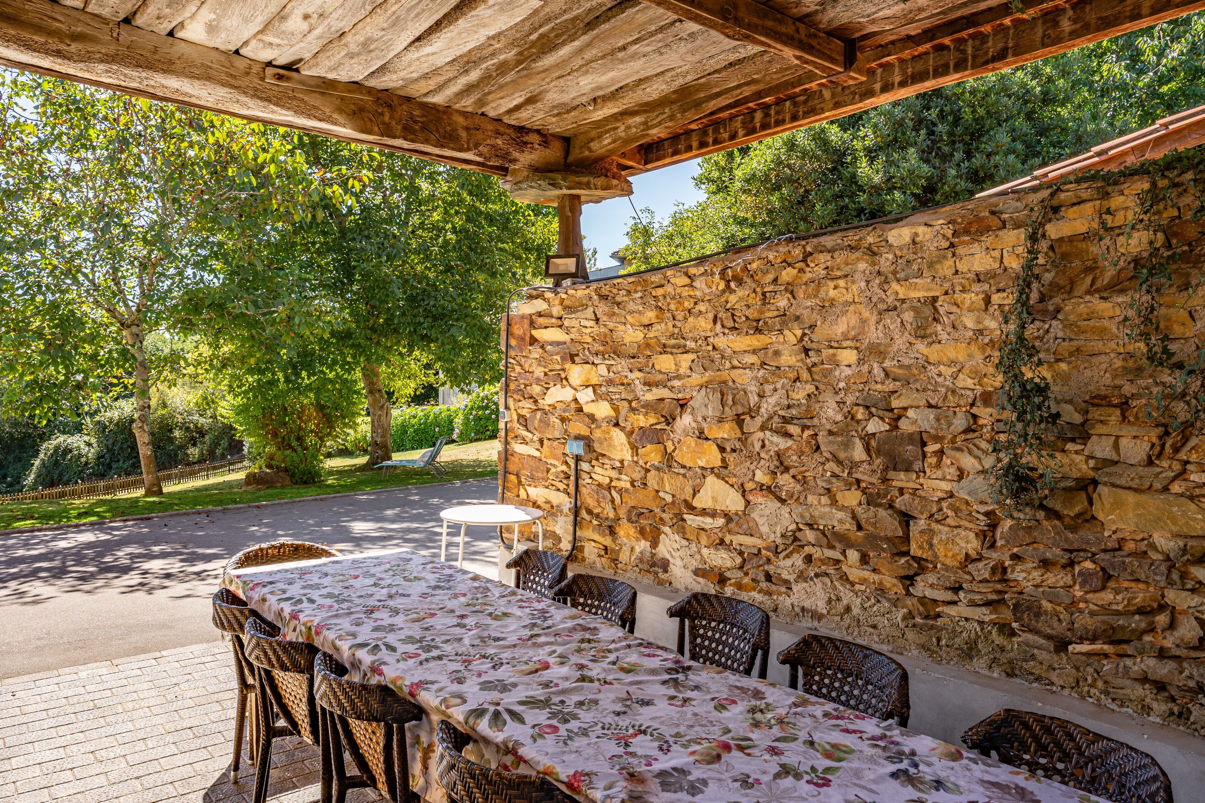 Un patio al aire libre con un muro de piedra, muebles de mimbre y una mesa con mantel floreado.