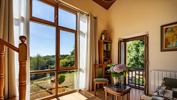 A room with a large window, wooden furniture, a chair, a small table with a vase, and a bookshelf. - Country House 'Hortensia' with Mountain View, Private Terrace and Wi-Fi (Asturias)