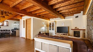 A spacious living area with a wooden ceiling, a sofa, a television, and a fireplace. - Country House 'Hortensia' with Mountain View, Private Terrace and Wi-Fi (Asturias)
