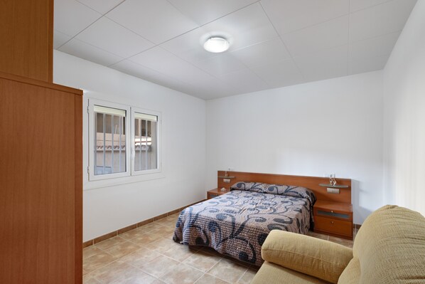 A bedroom with a bed, a nightstand, a wooden wardrobe, and a window.