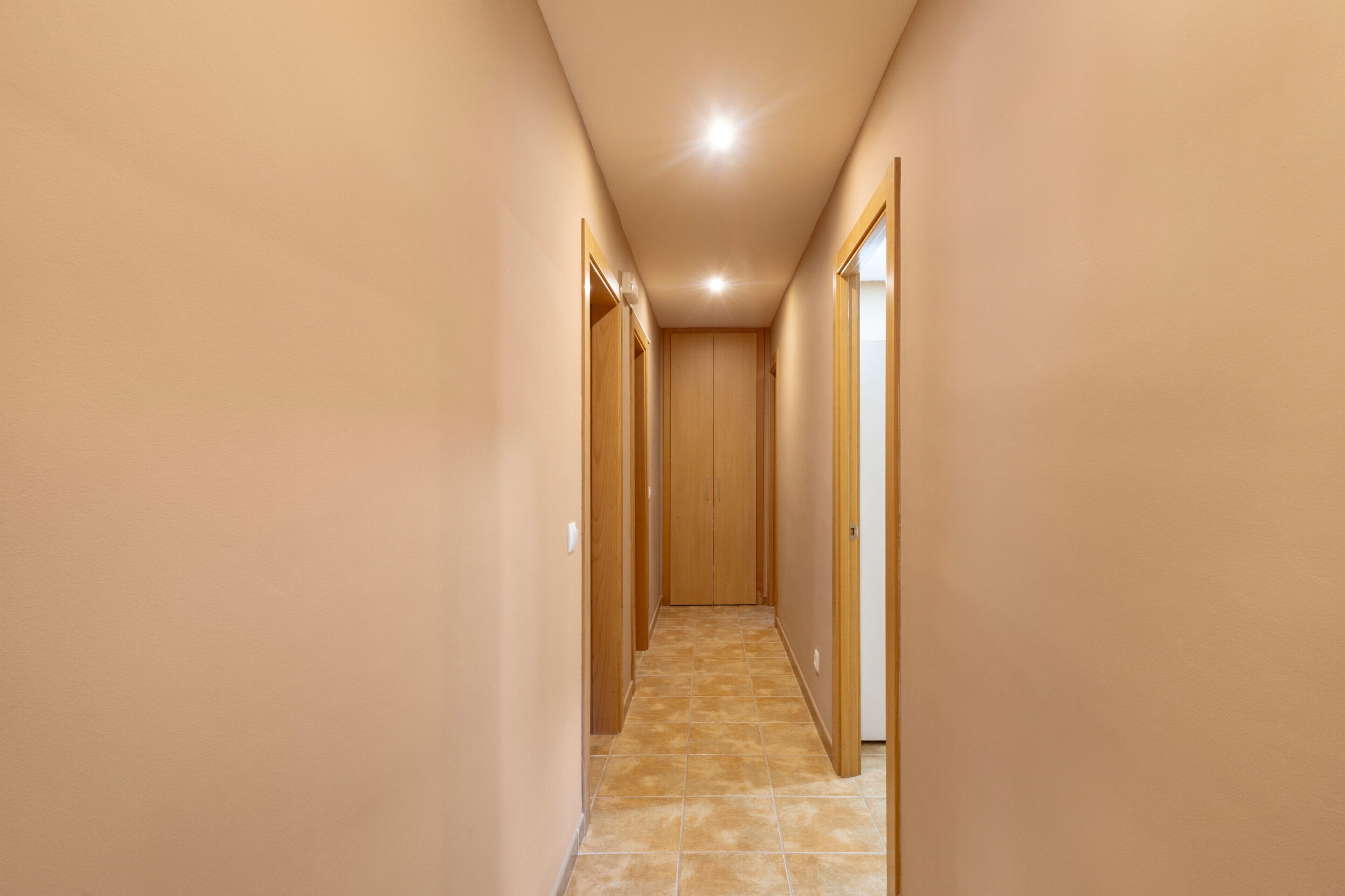 Un pasillo estrecho con puertas de madera a ambos lados, que da a una habitación.
