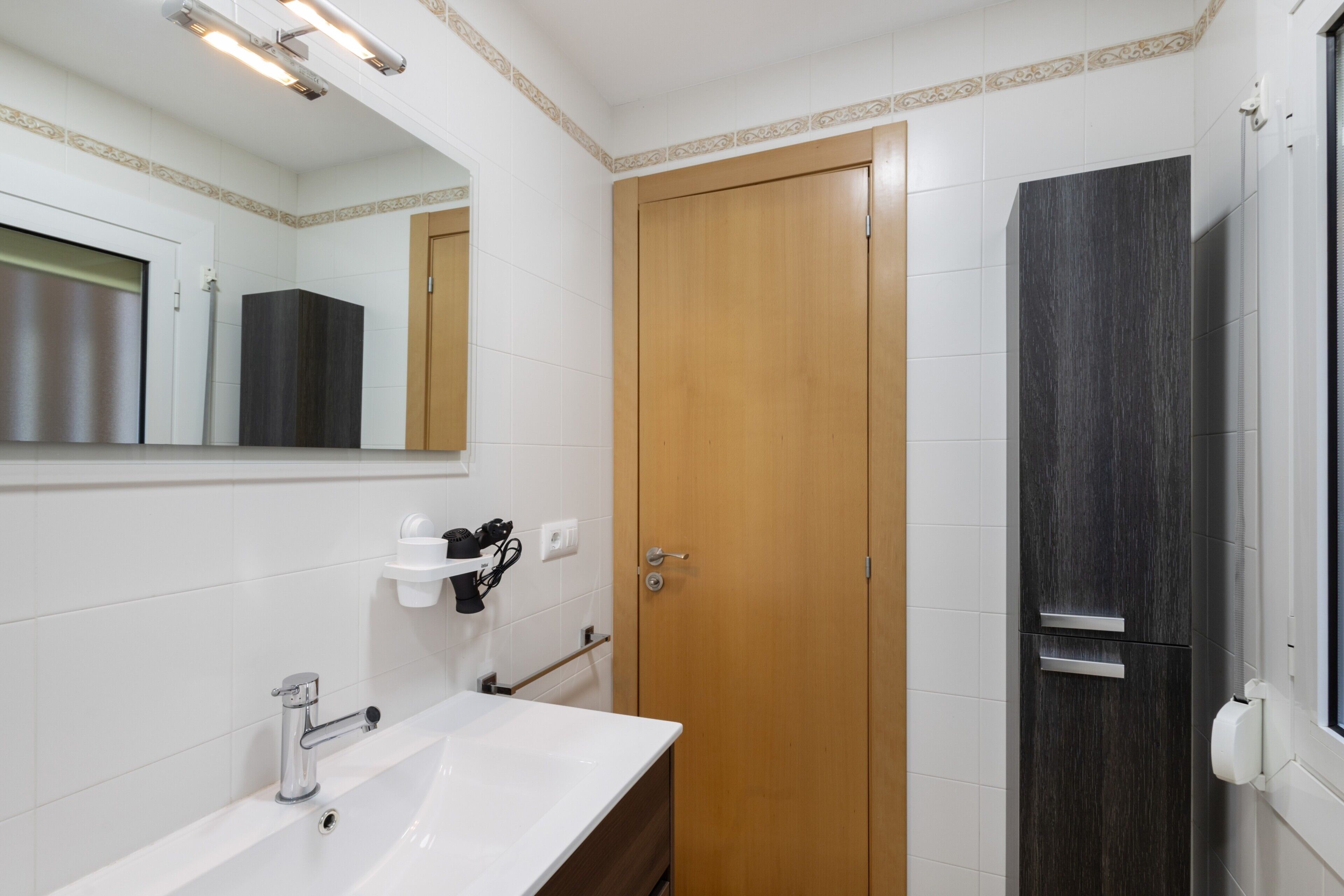 Een badkamer met een wit wastafel, een houten deur en een spiegel.