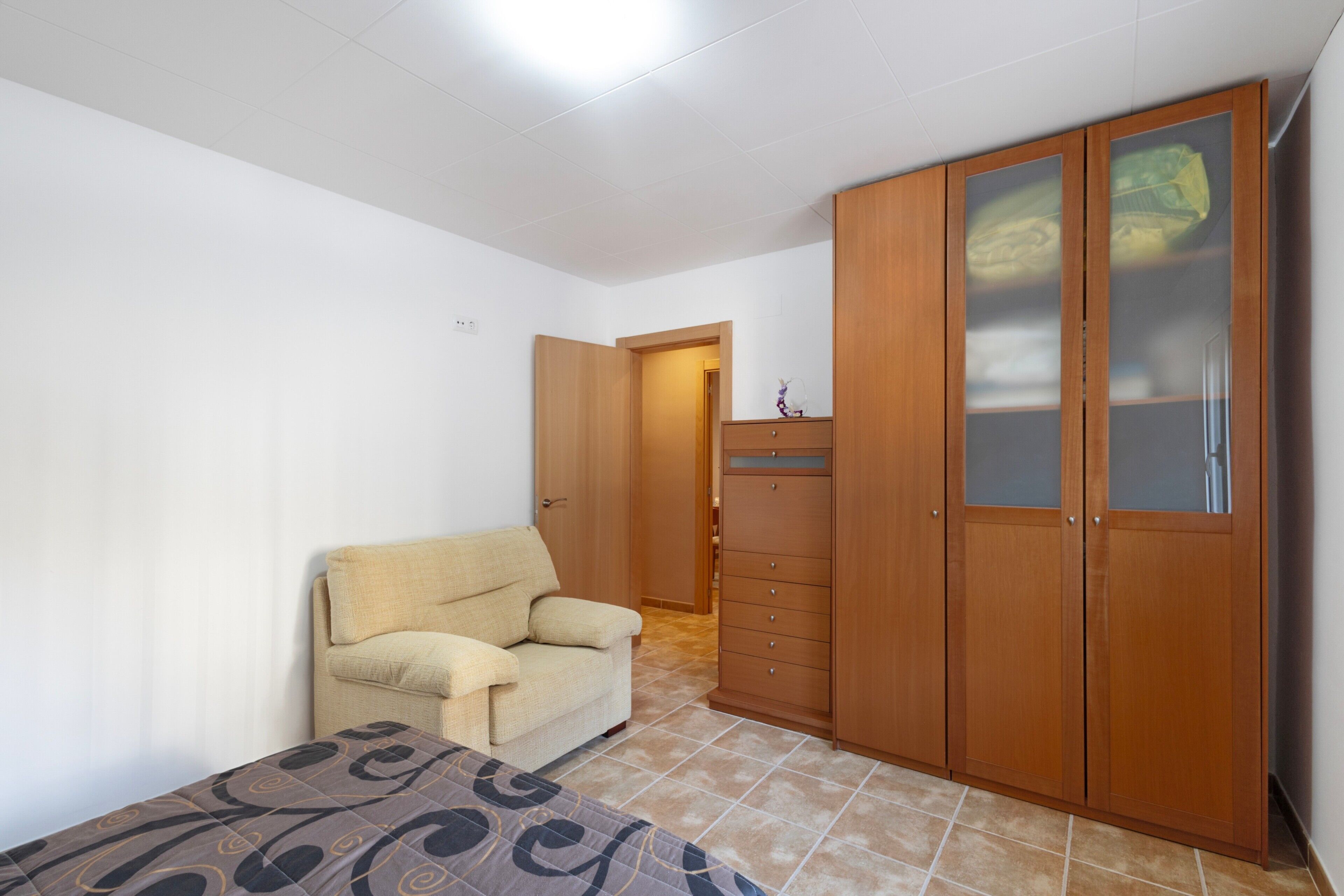 Un dormitorio con cama, sofá, armario y puerta que da a otra habitación.